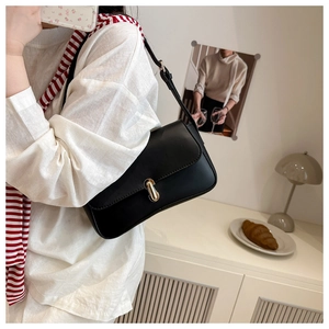 Detail view of a black leather shoulder bag with golden metallic clasp in a French chic setting