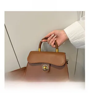 Detail showing vintage golden rotary lock and brown leather texture on handbag