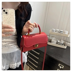 Detailed view of the red leather handbag featuring a golden circular metal twist lock clasp