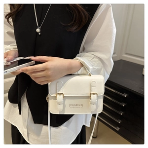 Close-up of white minimalist flap bag with golden buckles and textured leather surface