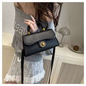 Close-up of a black leather handbag with a prominent golden circular twist-lock clasp