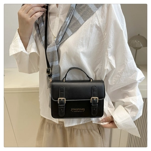 Detail shot of a black leather rectangular crossbody bag featuring elegant gold buckles