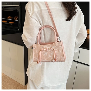 Detailed view of pink lace crossbody bag with pearl charms on a white shirt model
