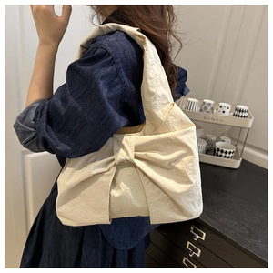 Détail d'un sac cabas en nylon blanc crème avec un grand nœud décoratif et texture plissée