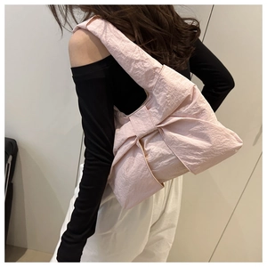 Side view of pink oversized bow shoulder bag with pleated texture on model