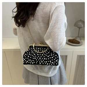 Detail of a vintage black shell bag with white pearls and a gold ring handle