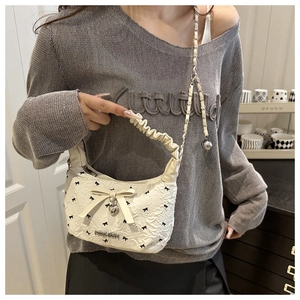 Detail of white textured crossbody bag featuring bow prints and silver heart pendant