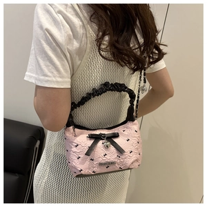 Détail du sac gaufré rose avec nœud noir, pendentif cœur et bandoulière en chaîne