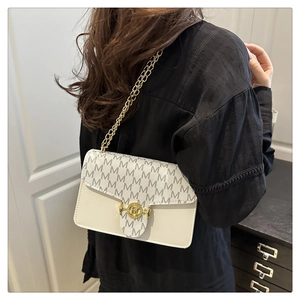 Detail of the golden chain strap and monogram flap on a cream crossbody bag