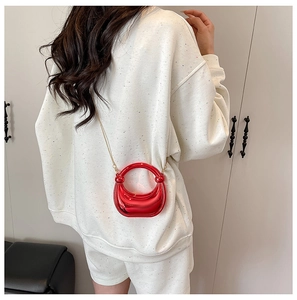 Mini bolso rojo metalizado con cadena dorada sobre una sudadera blanca de mujer