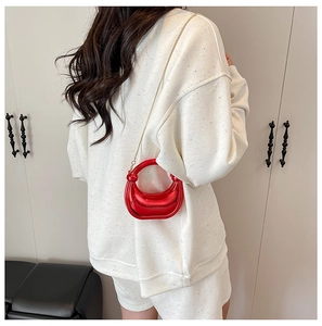 Detail of red metallic acrylic dumpling bag with gold chain strap on casual outfit