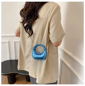 Close-up of bright blue acrylic dumpling bag with metal chain and round handle on model