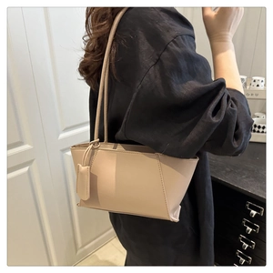 Détail du sac sous l'aisselle beige minimaliste avec fines bretelles et pendentif en cuir