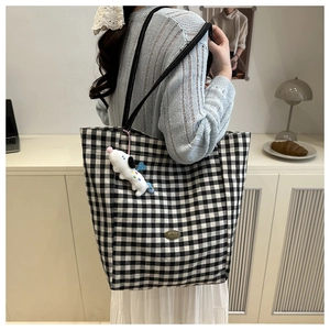 Detail of checkered canvas tote bag with a cute cartoon dog plush charm and metal tag
