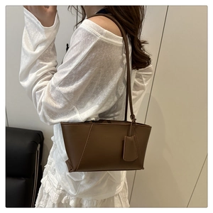 Model wearing a dark brown leather tote bag showing side view and trapezoid silhouette