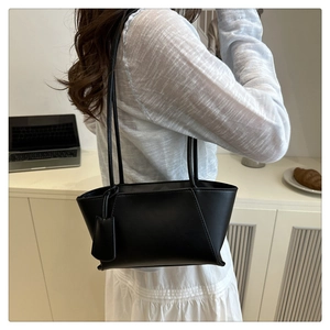 Détail d'un sac trapèze en cuir noir mat présenté dans un décor de bureau décontracté