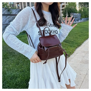 Detail of a dark brown glossy leather backpack with flap and drawstring closure outdoors