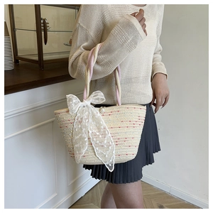 Detalle del bolso tipo cubo de paja con asas rosas y un gran lazo de encaje blanco