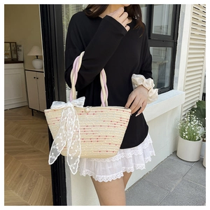Close-up of woven straw tote bag featuring a large white lace bow and twisted rope handles