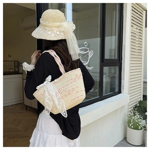 Detail of straw tote bag with pink stitching, white lace bow, and pearl decoration