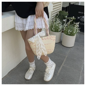 Detail view of woven straw beach bag featuring colorful fiber dots and a lace bow charm