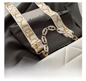 Detail of white geometric embossed handbag with gold chain and trendy patterned strap