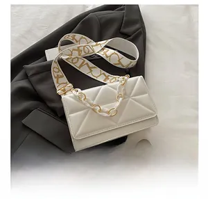 Detail of white quilted crossbody bag with gold chain and patterned fabric strap