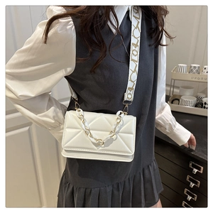 Detailed view of white quilted crossbody bag with gold chain strap and patterned wide strap