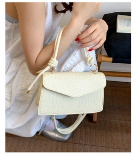Détail du sac crème à texture tissée avec poignée nouée et anneaux en métal doré