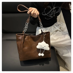 Detail of a brown patchwork leather tote bag with silver chain strap and cloud pendant