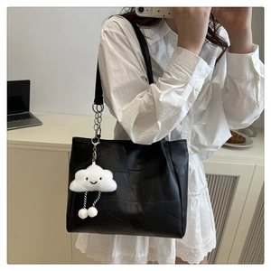 Detail of black patchwork tote bag featuring a plush white cloud charm on the shoulder strap