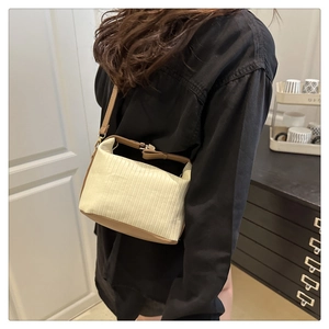 Détail d'un sac vintage rayé crème avec bordure en cuir marron porté par un modèle