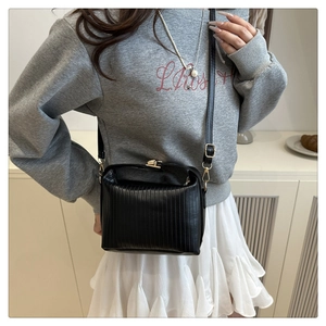 Detail of black pleated crossbody bag featuring a golden metal clasp and leather strap