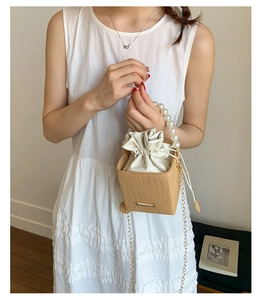 Detail of khaki woven bucket bag with large pearl handle and gold chain strap