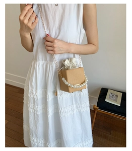 Detail of woven straw bag featuring elegant pearl handle and gold chain shoulder strap