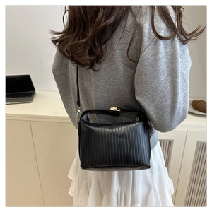 Chic black pleated handbag with gold clasp worn by a model in a minimalist setting
