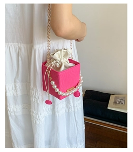 Pink quilted bucket bag featuring a pearl handle, gold chain strap, and drawstring liner