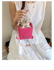 Detail of pink woven crossbody bag featuring a pearl handle and gold chain strap