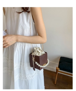 Detail of a brown bucket bag featuring a large pearl handle and drawstring closure