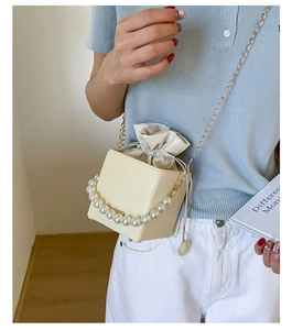 Detail of cream crossbody bag featuring pearl handle and metallic chain strap