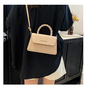 Détail d'un sac bandoulière beige trapèze avec poignée tressée et accents dorés