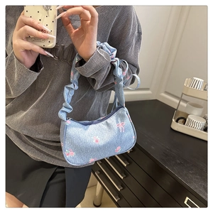 Detail of denim crescent bag with floral print and ruched handle carried by a model
