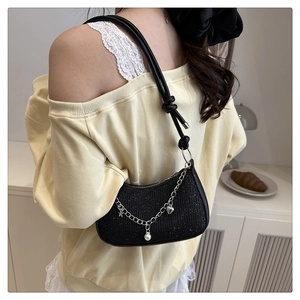 Detail of black glossy baguette bag with silver chains, pearl charms and star pendants