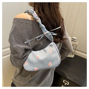 Detail of light blue floral denim bag with ruffled strap and bow accents on a model