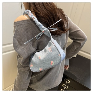 Close-up of blue denim underarm bag with pink rose prints and twisted rope strap detail
