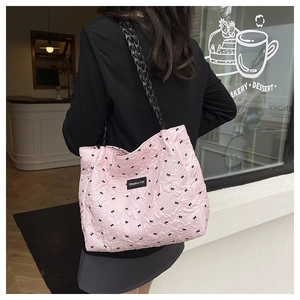 Pink quilted tote bag with black bow print and woven straps shown on model