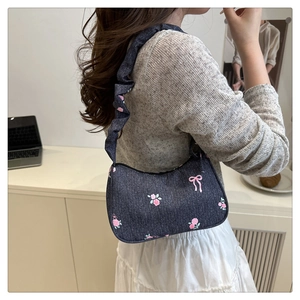 Detail of blue denim shoulder bag with floral print and pleated strap shown on shoulder