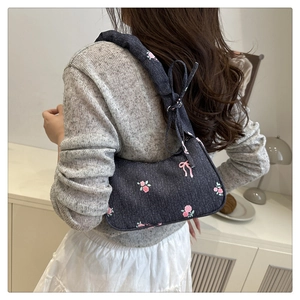 Detail of dark blue denim underarm bag with pink rose and bow prints on shoulder