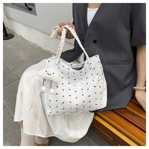 Close-up of white pleated tote bag featuring black bow patterns and a plush cloud charm