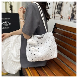 Close-up of a white textured tote bag with black bow prints and a cloud plush charm